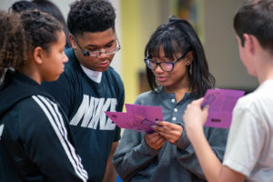 Group of teens looking at and reading off of scenario cards as part of a training program
