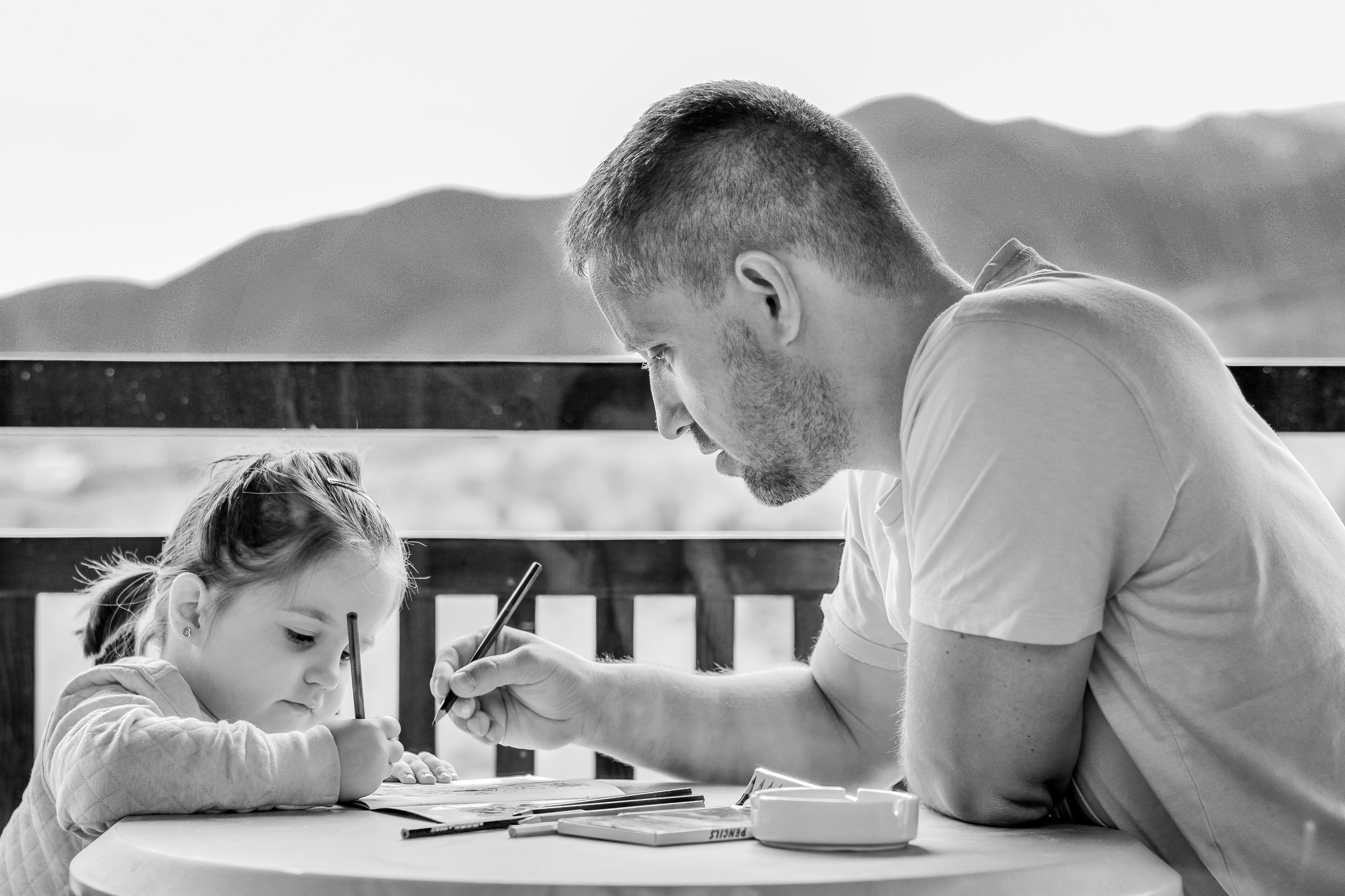 A young girl writing with her father at a table