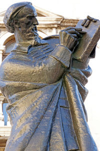 Photo of a bronze statue of a standing man in robes  writing on a tablet