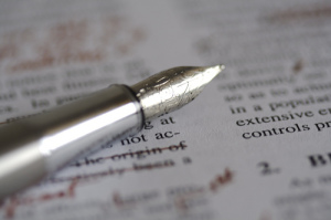 Photo of a fountain pen sitting on top of a printed page.  Editing marks have been made in red on the page