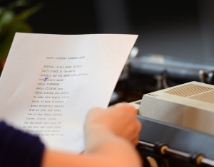 Photo looking over the shoulder of a person holding a piece of paper with a typed poem on it.  It has been edited in one spot with handwriting