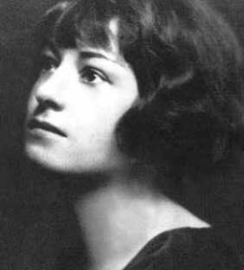 Black and white head shot of Dorothy Parker.  She has ear-length dark hair waved around her face, and short bangs.  She wears a dark top covering her shoulders, with an open neck.  She stares off to the left, looking up. 