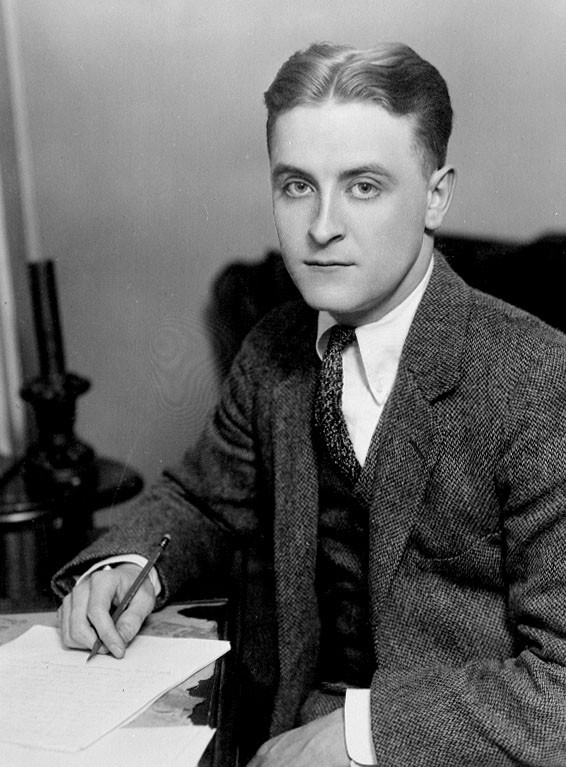 Black and white photograph of Fitzgerald as a young man, seated at a desk with pen in hand, looking at the camera