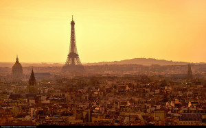 Photo of Paris skyline, looking down from a distant hill.  The Eiffel Tower stands dominant towards the left.  The sky is bright yellow, and the city is hazy amber.