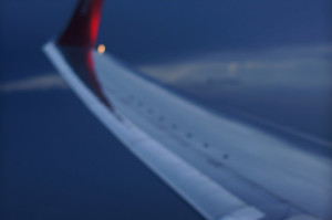 Photo of a wing of a plane, taken from inside the cabin.  The sky is dark and the focus is soft.
