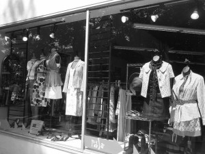 Black and white photo of a department store window display, showing several outfits on headless dressing dummies