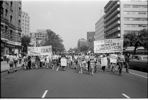 Black and white photo of a protest march in a city street.  Protesters are primarily female.  Signs held read 