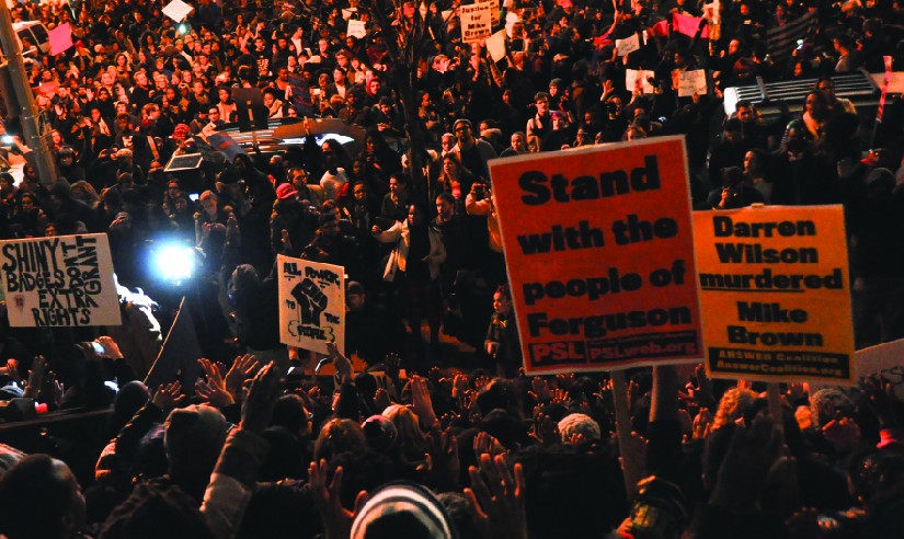 An image of a large crowd of people, some holding signs that read 