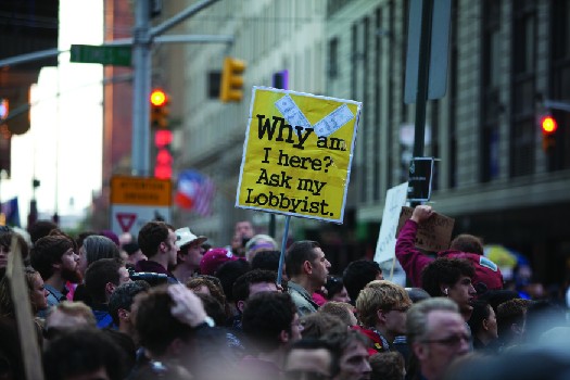 An image of a crowd of people, one of whom holds a sign that reads 