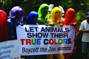 An image of a group of six people, each one painted a different color, holding a sign that reads