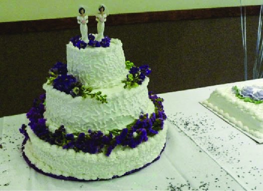 A photo of a cake with three tiers. Two human figurines appear on the top tier.