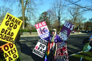 A photo of people holding signs. The signs have messages like Thank God for Dead Soldiers and Soldiers Die for Fag Marriage.