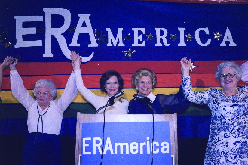 A photo of Rosalynn Carter and Betty Ford speaking at a rally in favor of the Equal Rights Amendment. Signs on stage read 