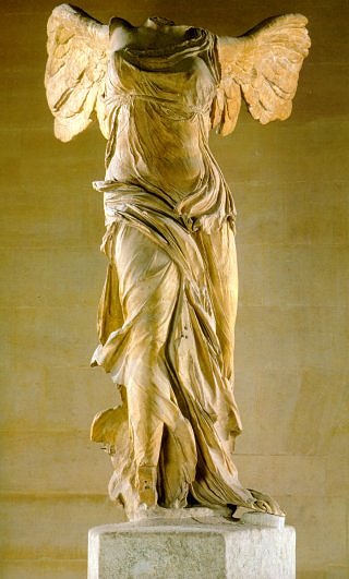 A marble sculpture of a winged woman. Over time, her head and arms have been lost. Her draping clothes appear light and flowing, despite the hard medium of the sculpture. 