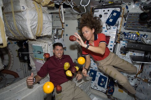 Photograph of Astronauts Aboard the Space Shuttle Endeavour. Two astronauts are seen, along with apples, oranges and pears, 