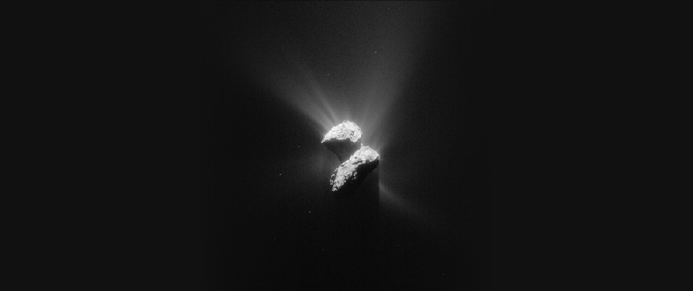 Image of Comet Churyumov-Gerasimenko (67P). Two lobes of this irregularly shaped object are illuminated by sunlight coming from the upper left. Bright streaks of material are seen radiating away from the sunlit surfaces of the comet. These streaks are not seen coming from the shaded portions.