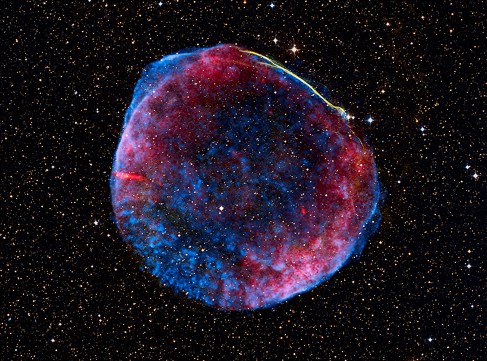 Multi-wavelength Image of SN 1006. This nearly perfect spherical bubble of gas is seen here in X-rays (blue), visible (white-yellow) and radio light (red) against the background stars of the Milky Way.
