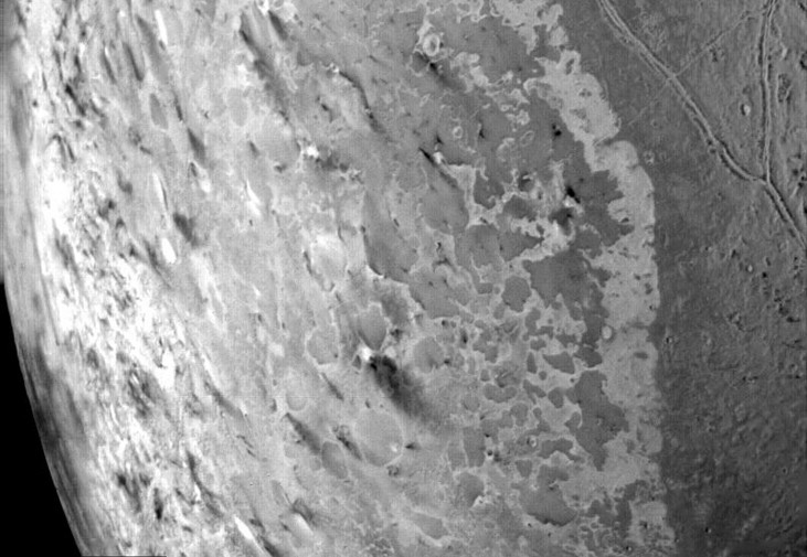 A close-up image of Triton’s geysers, with long trains of dust in the lower right.