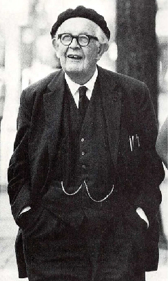Jean Piaget in his older years, standing with his hands in his pockets in a black suit, tie, and vest. He's wearing glasses and a beret.