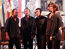 Five men singing around a microphone.