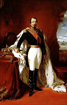 Portrait of Napoleon III. He is dressed in black and white in front of a red wall. 