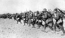 A line of men in the sand with bayonets.