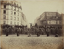 An image of a barricade in the Paris commune. Crowds of people are gathered. 