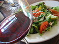 A glass of red wine next to a plate of salad. 