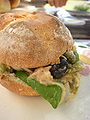 Image of pan bagnat, a sandwich with white bread, meat, and salad. 