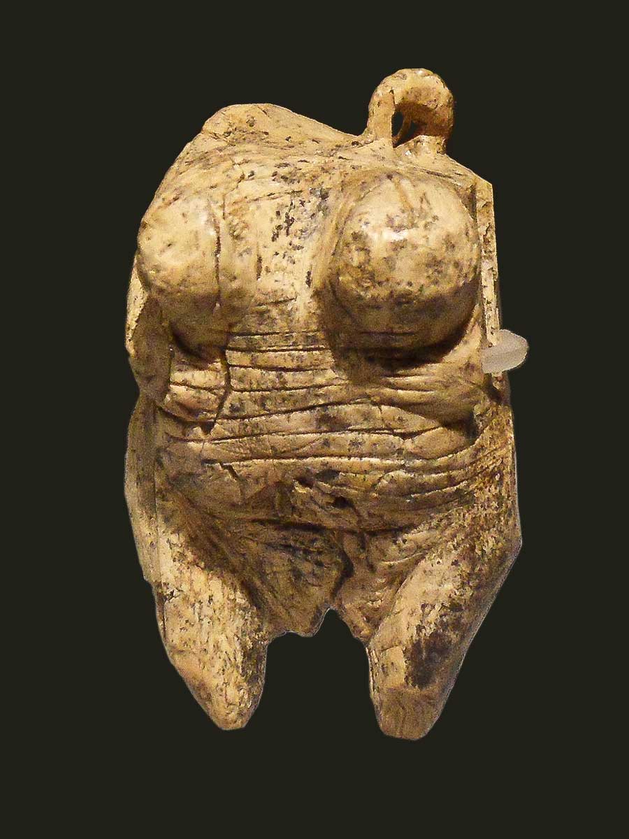 Image of the Venus of Hohle Fels. What remains of the hewn statuette are etchings across her pronounced torso as well as an accentuated bust to emphasize her child-bearing capabilities.