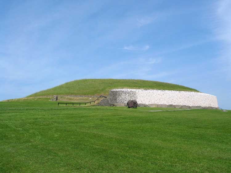 Picture of the Newgrange Monument. The perspective captures the mound-like structure rising from the lush green pasture.