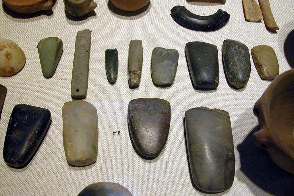 An array of Neolithic artifacts, including bracelets, axe heads, chisels, and polishing tools.