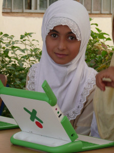 Iraqi girl in headscarf sits with a laptop.