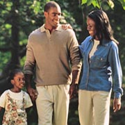 A smiling man and woman take a walk with their young daughter.