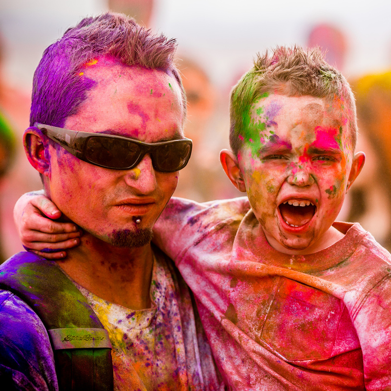 A father and son smile and shout after finishing an exciting race called The Color Run. Both are covered from head to toe in many shades of brightly colored powder.