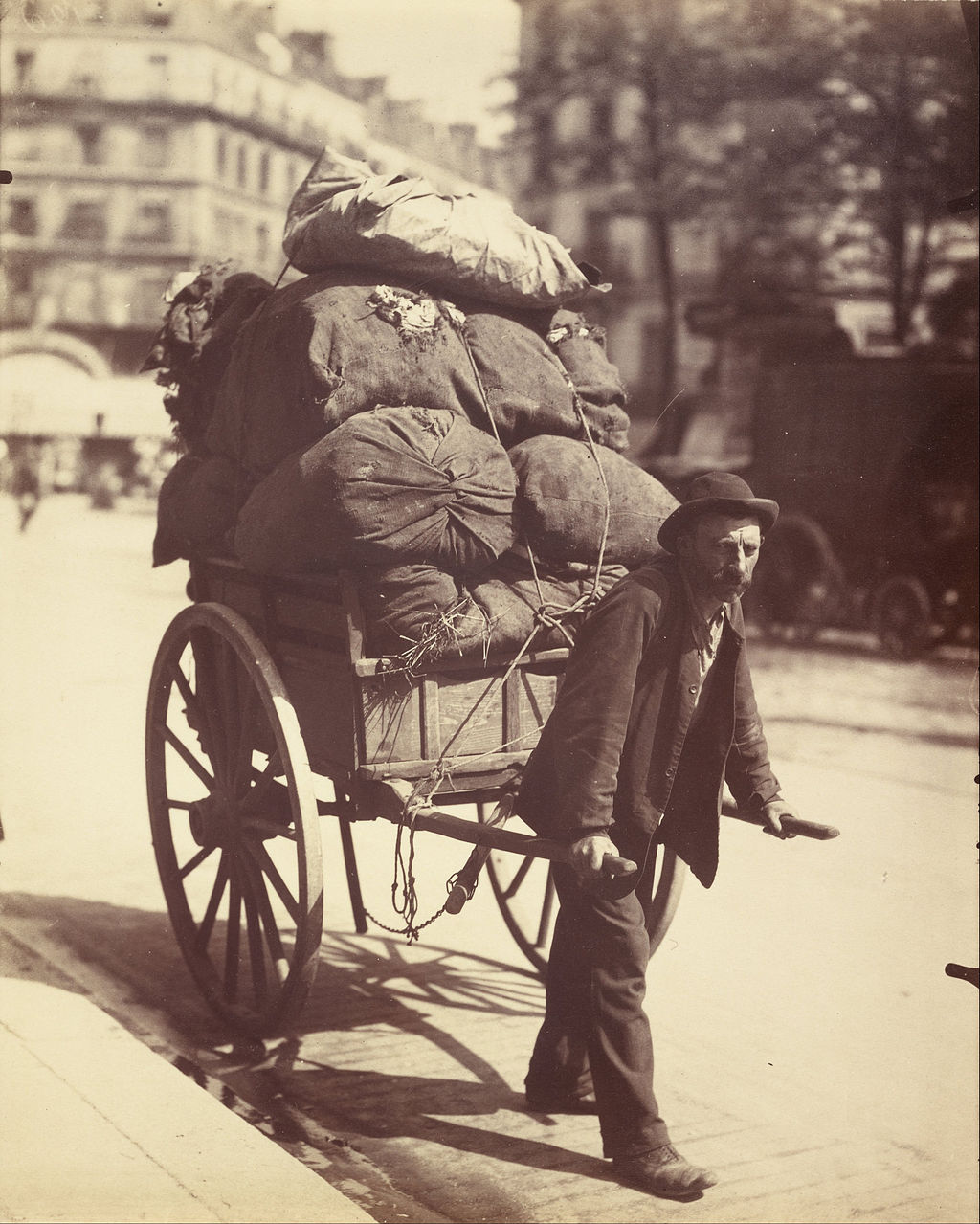 Man on a Paris street pulling a two-wheeled handcart loaded with sacks of old rags