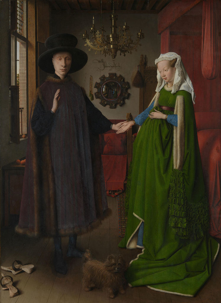Well-dressed man and woman standing slightly apart, holding hands. Woman is visibly pregnant.
