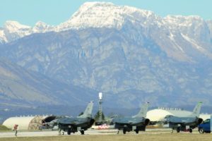 An image of several grounded fighter jets, with a mountain range in the background.