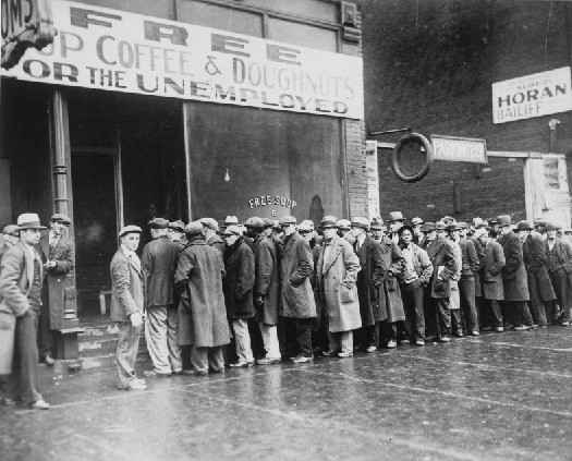 Photo shows a line of people in long coats and hats standing in line outside a building with a sign that states