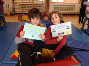 Photo of two children sitting on the floor, holding up certificates about belonging to Trampoline Club.