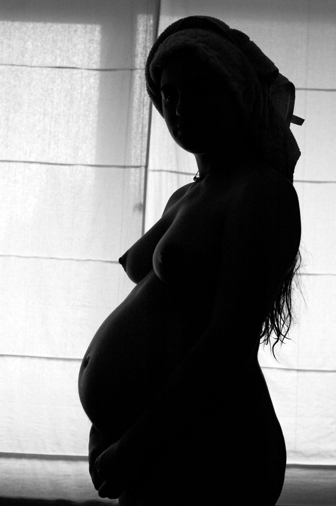 This photograph is a silhouette of a nude, pregnant woman.