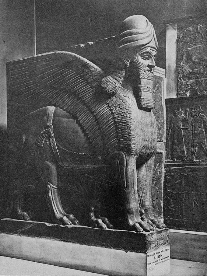 Black and white photo depicts large sculpture of man-headed winged lion.