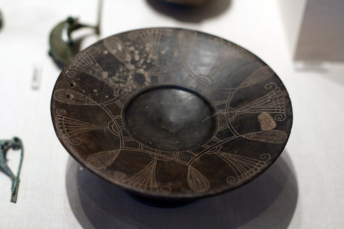 This is a photo of a bucchero Etruscan plate. Its rim is decorated with an abstract design.