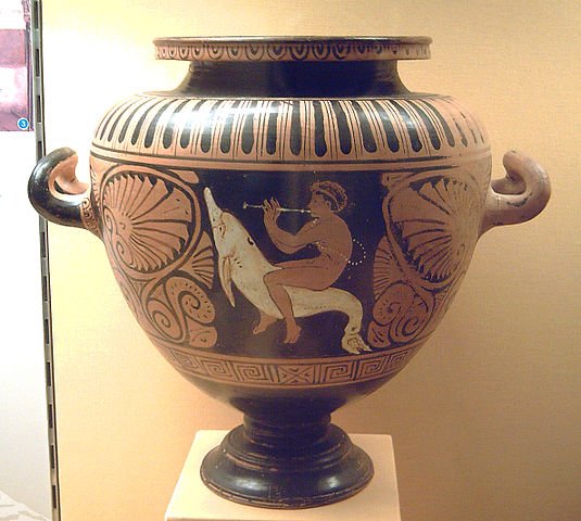This is a photo of an Etruscan red-figure stamnos. In the center is a mythological scene of a man or god riding a dolphinlike creature. The sides feature a decorative floral motif.