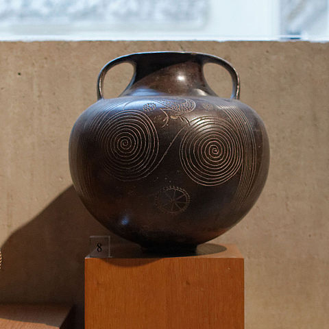 This is a photo of Etruscan pottery. It is a round vase with a thin neck and handles. It is decorated with two spirals and a stylized bird.