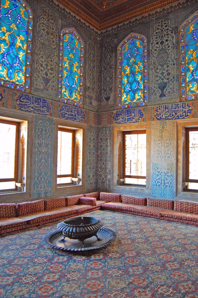 This photo shows the carpet and interior of the Harem room in Topkapi Palace, Istanbul. It shows intricate blue and yellow floral stained glass windows and patterned carpet.