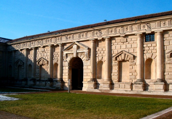 Picture of an outside wall of the palace from the courtyard. The colonnaded walls are a tan color and decorated by deep niches and blind windows.