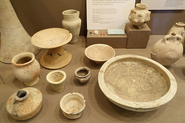 Photograph depicting a large pottery collection featuring a small pedestal, cups and bowls in various sizes, and a large round plate or tray.