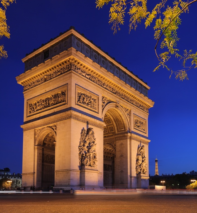 Photo of the Arc de Triomphe lit up at night. There are two enormous archways leading inside, and it is intricately decorated on the outside.