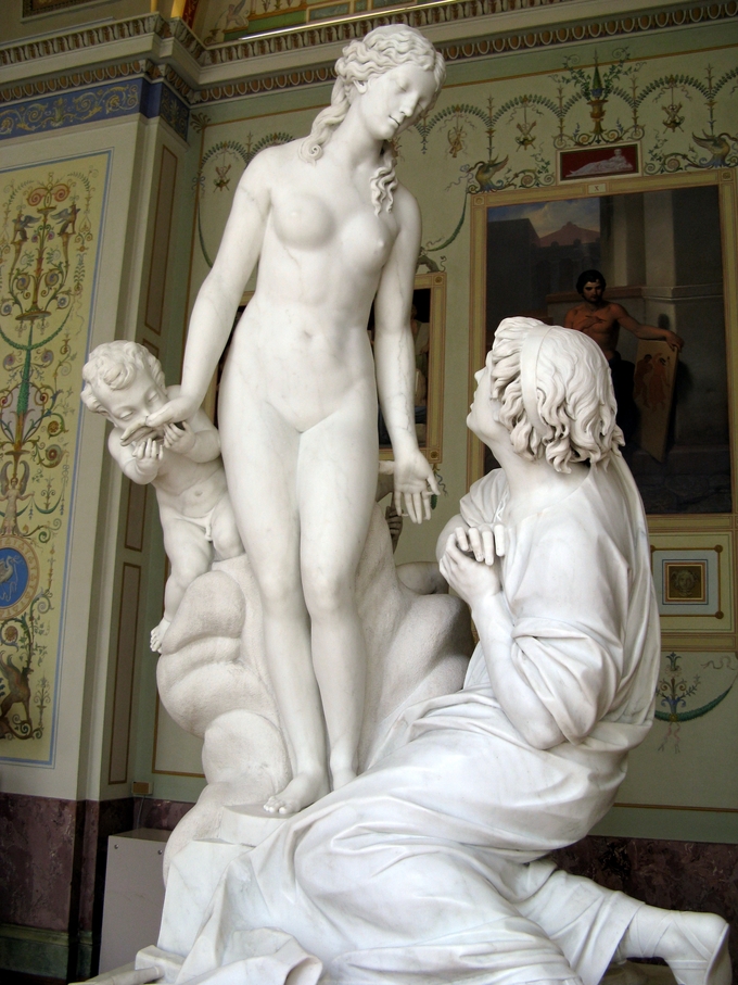 Sculpture depicts Pygmalion on his knees, falling in love with a sculpture of a woman. A cherub kisses the hand of the woman.